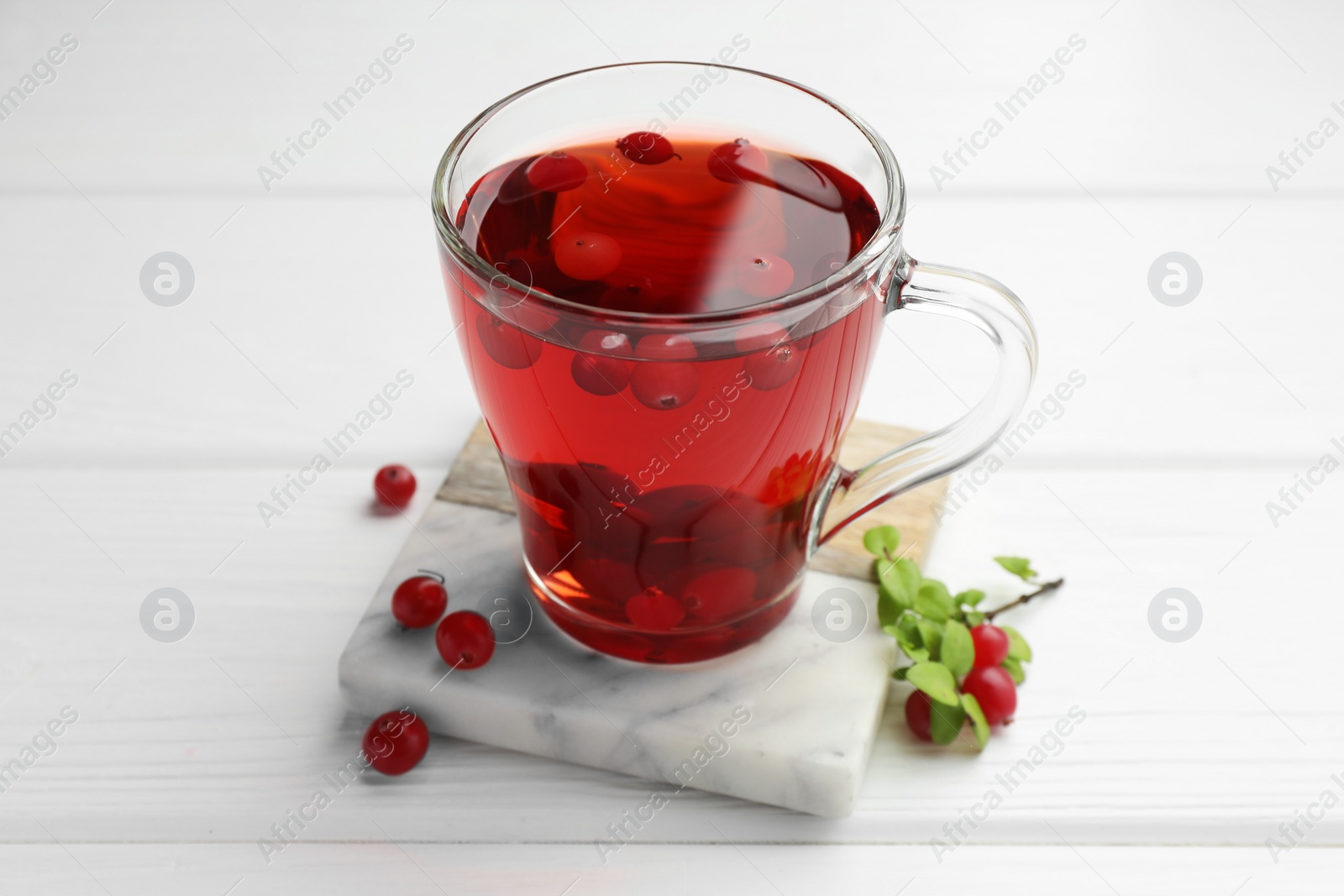 Photo of Tasty hot cranberry tea in glass cup and fresh berries on white wooden table