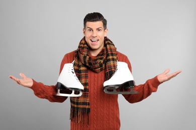 Emotional man with ice skates on grey background