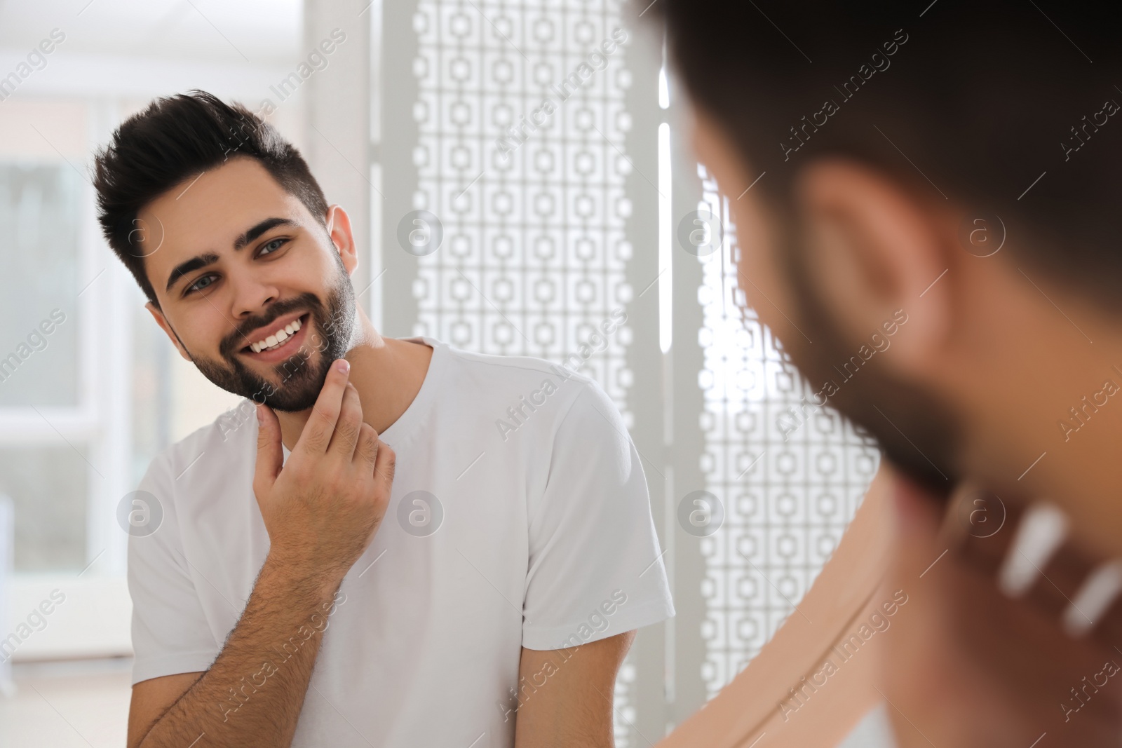 Photo of Handsome young man after shaving near mirror in bathroom