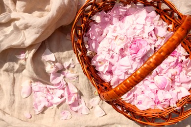 Photo of Wicker basket of beautiful tea rose petals on beige fabric, flat lay