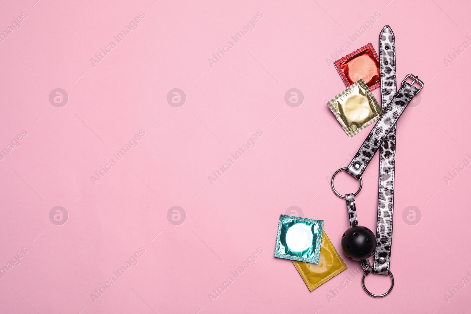 Photo of Ball gag and condoms on pink background, top view with space for text. Sex game