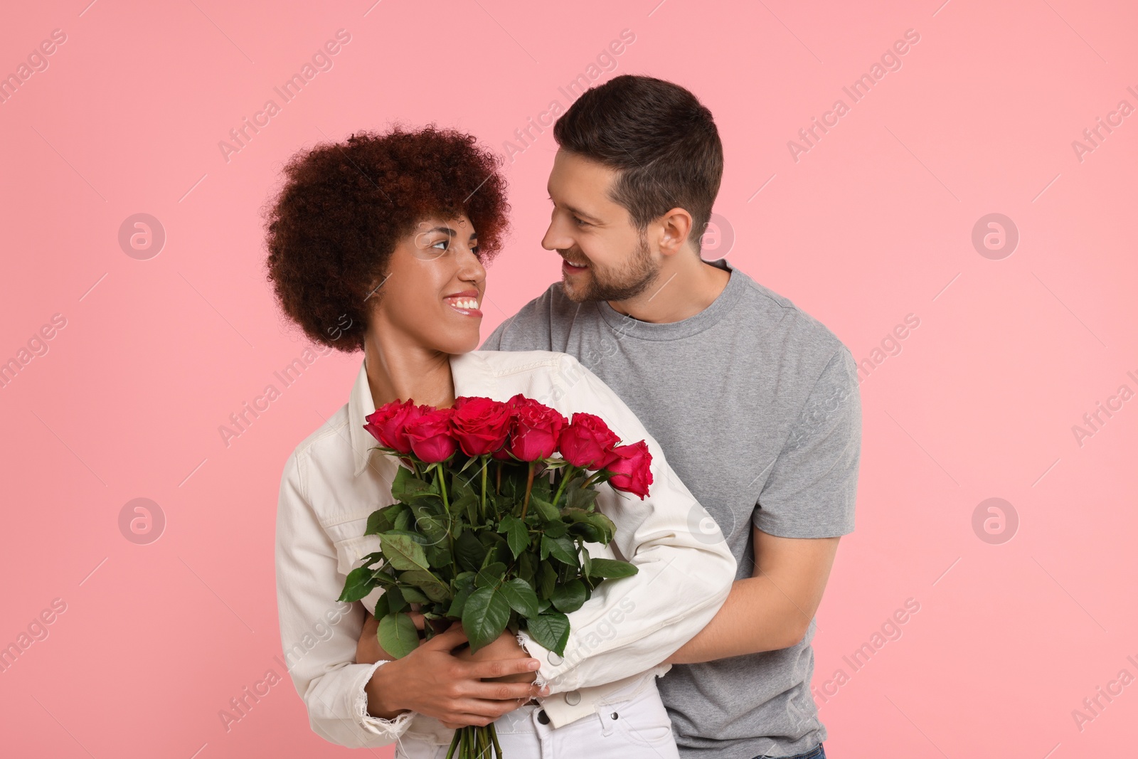 Photo of International dating. Lovely couple with bouquet of roses on pink background