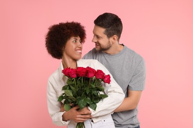 Photo of International dating. Lovely couple with bouquet of roses on pink background