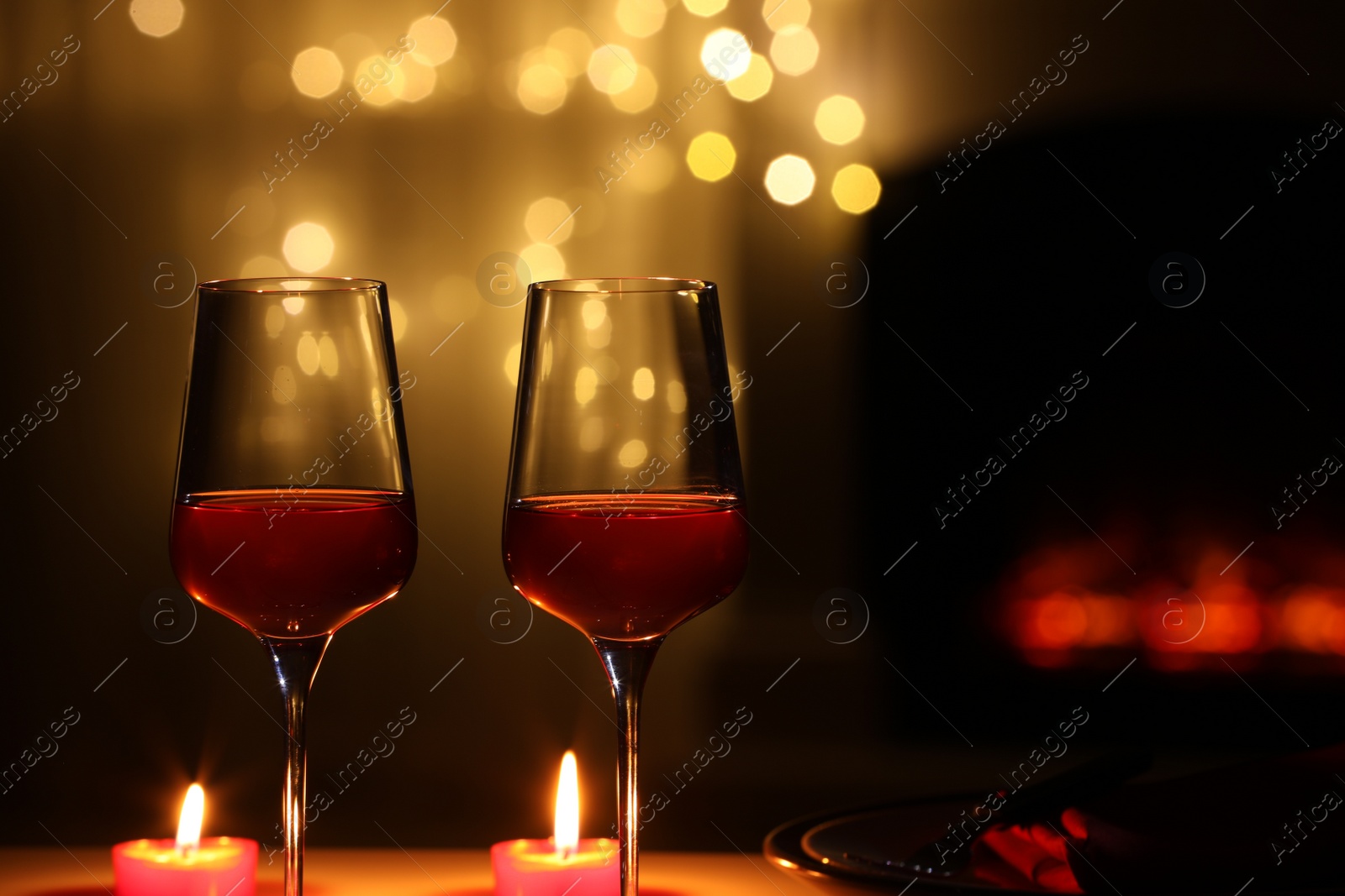 Photo of Glasses of wine and candles against blurred lights, space for text. Romantic dinner