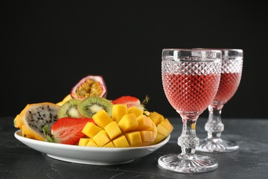 Delicious exotic fruits and glasses of wine on black table