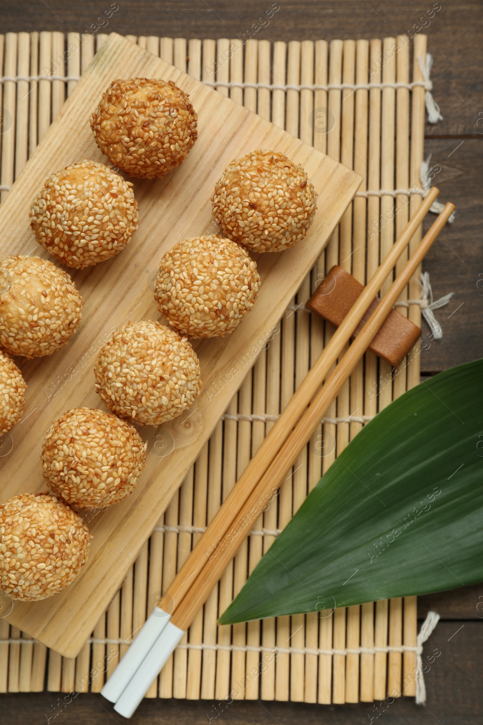 Photo of Delicious sesame balls, green leaf and chopsticks on wooden table, flat lay