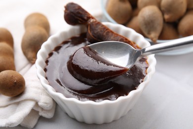 Photo of Taking tasty tamarind sauce with spoon from bowl on white table, closeup