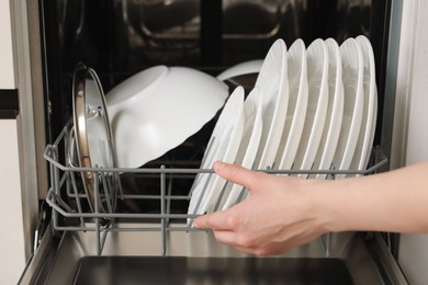 Woman loading dishwasher with plates indoors, closeup