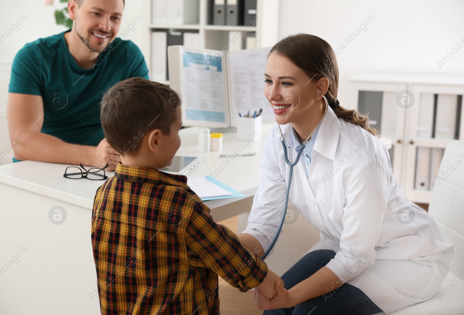 Photo of Father and son visiting pediatrician. Doctor examining little patient with stethoscope in hospital