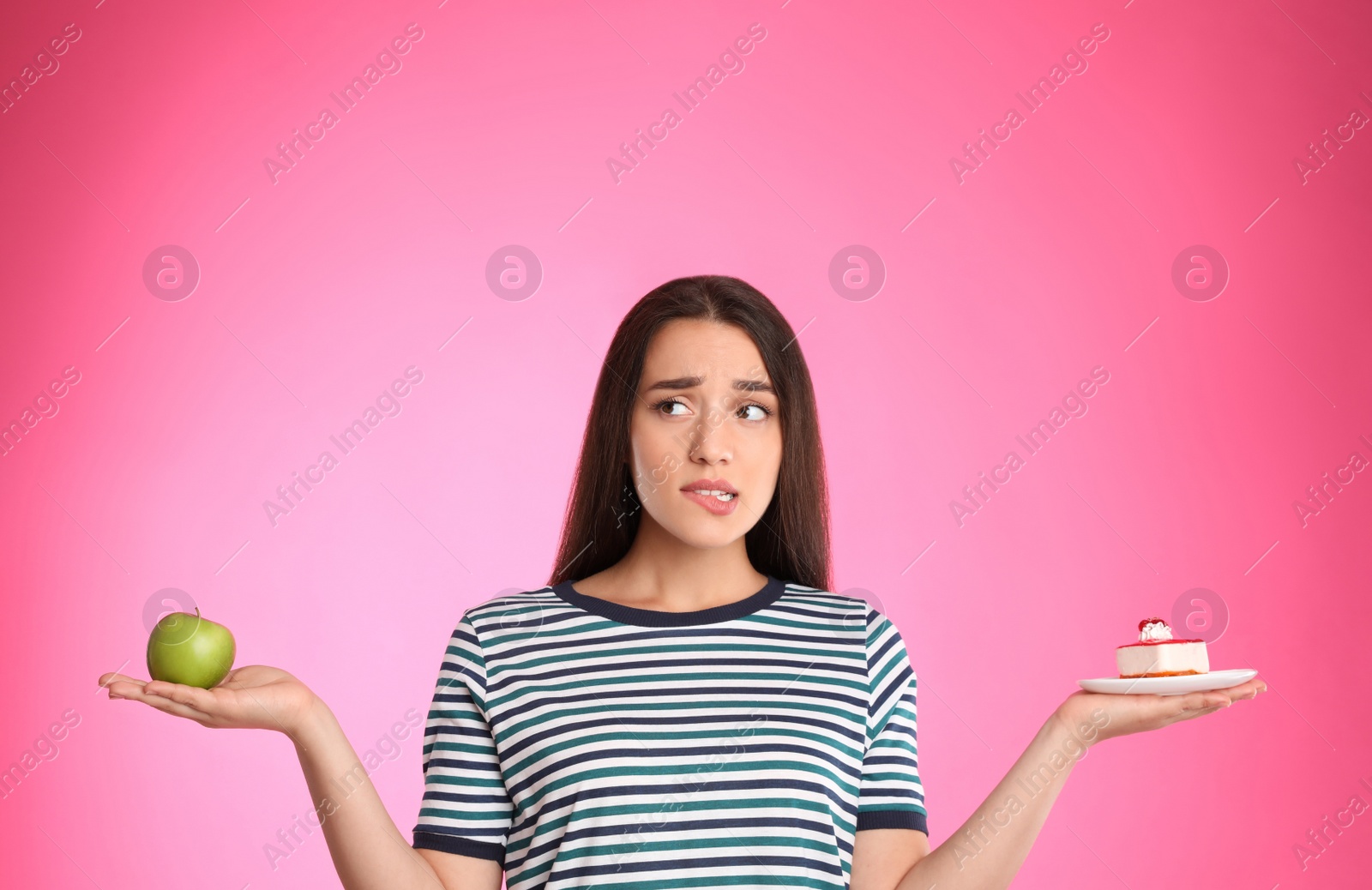 Photo of Concept of choice. Doubtful woman holding apple and cake on pink background