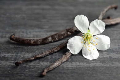Photo of Aromatic vanilla sticks and flower on wooden background, closeup