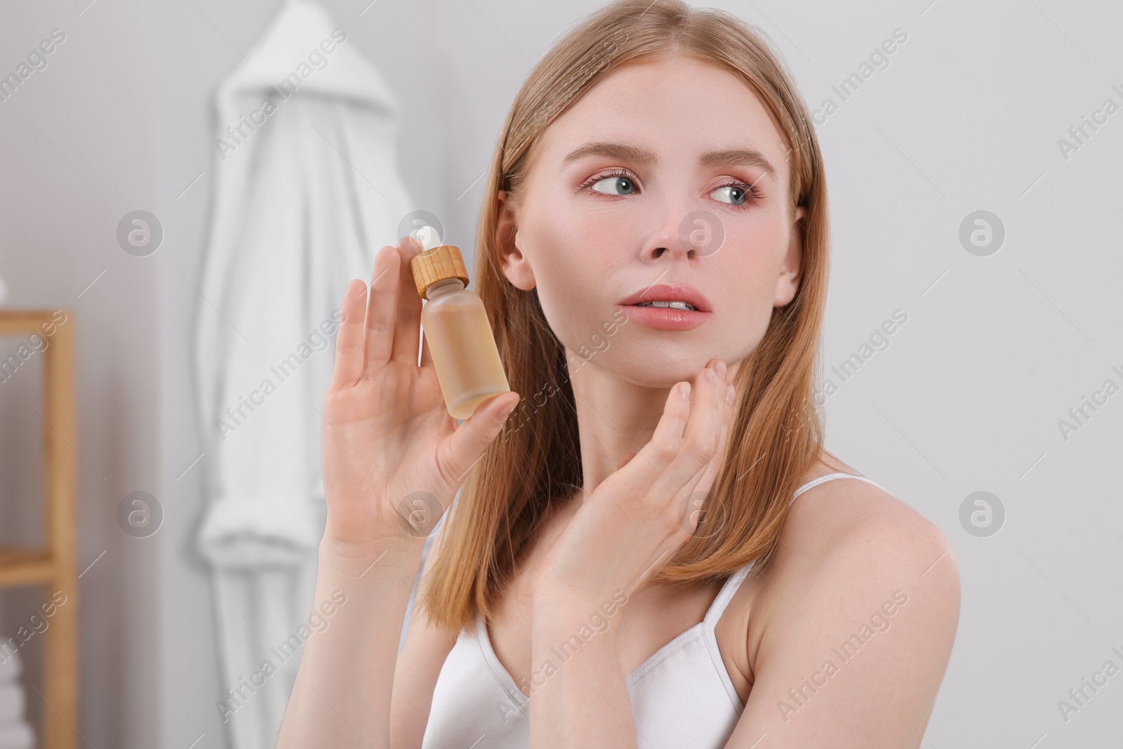 Photo of Young woman with bottle of essential oil in bathroom