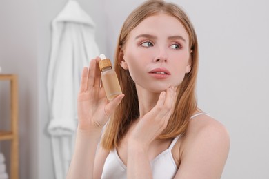 Young woman with bottle of essential oil in bathroom