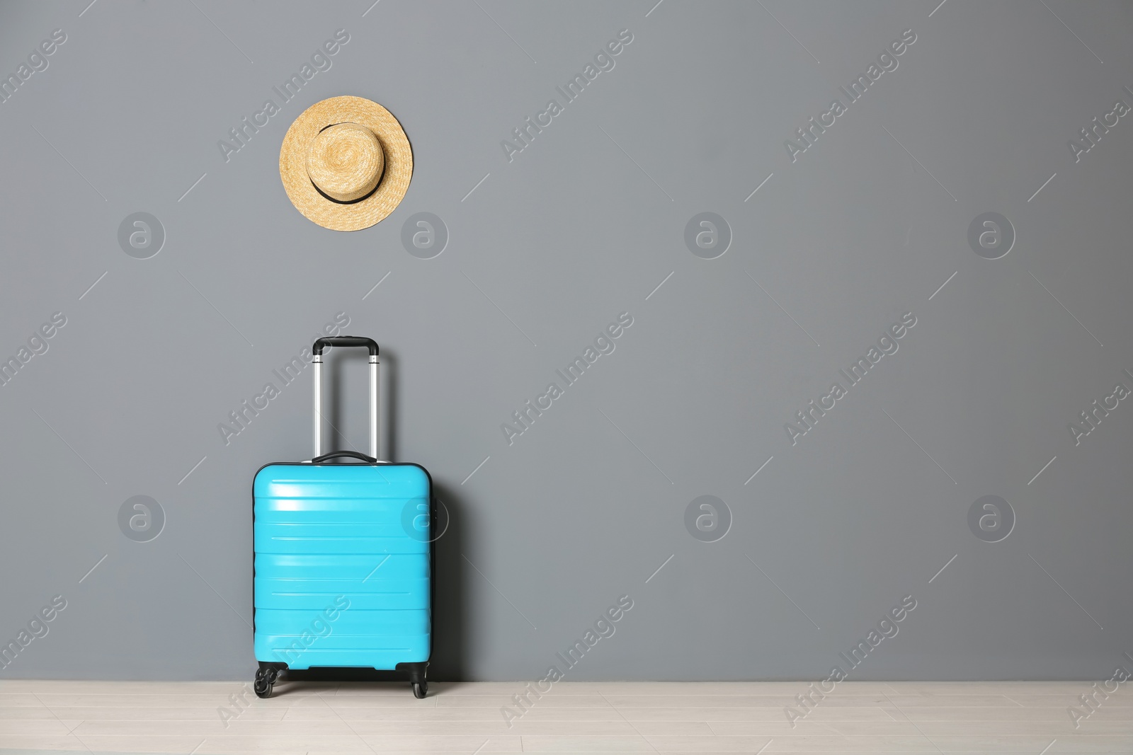 Photo of Suitcase with hat near gray wall. Space for text