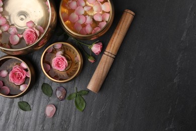 Photo of Tibetan singing bowls with water, beautiful rose flowers and mallet on gray table, flat lay. Space for text