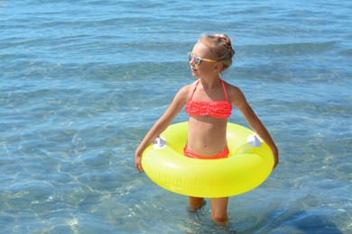 Photo of Happy little girl with inflatable ring in sea on sunny day, space for text