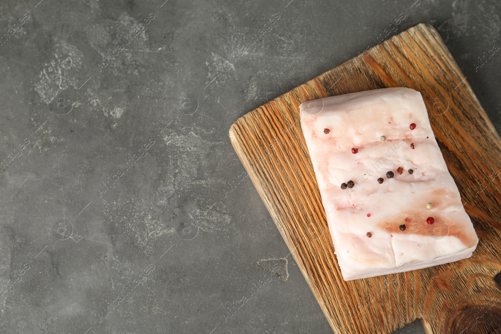 Photo of Board with pork fatback on grey stone background, top view. Space for text