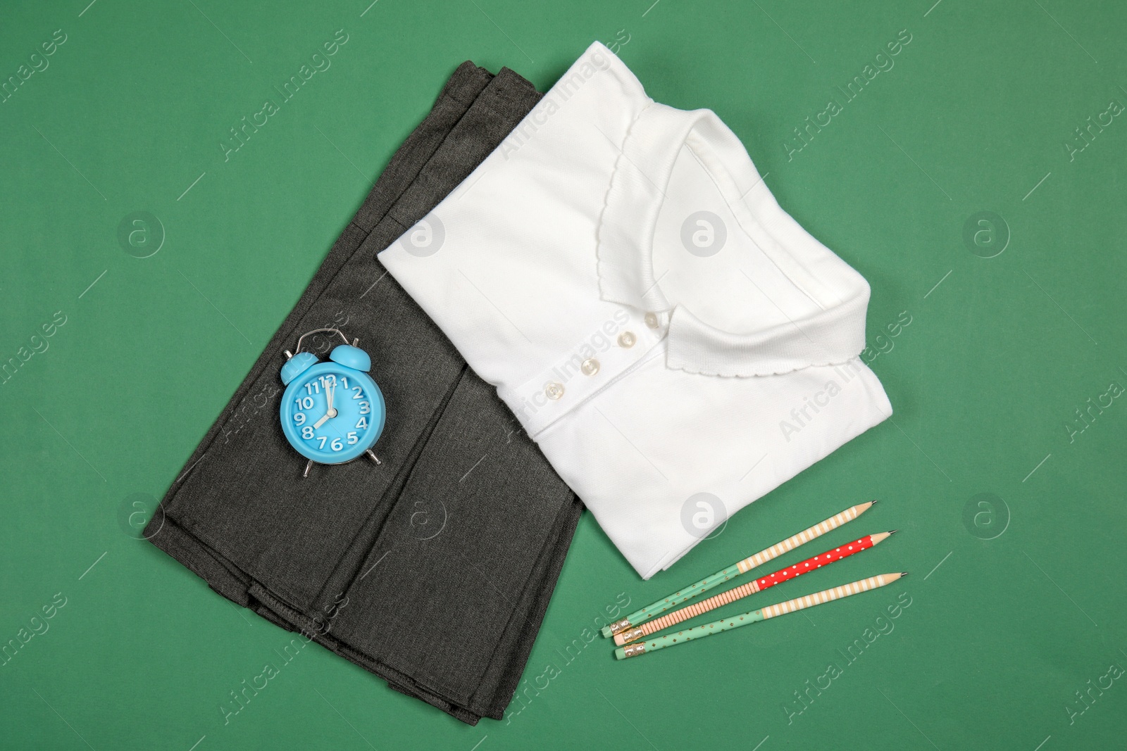 Photo of School uniform for girl and alarm clock on color background, top view