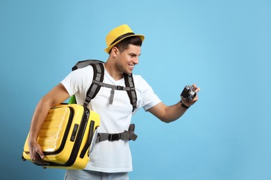Photo of Male tourist with travel backpack, suitcase and camera on turquoise background