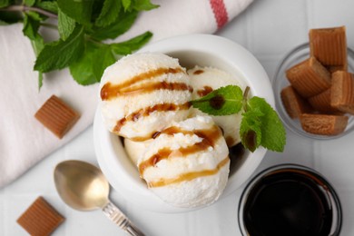 Photo of Scoops of tasty ice cream with mint, candies and caramel sauce on white tiled table, flat lay