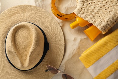 Photo of Straw hat, sunglasses, towel and bag with sunscreen on sand, flat lay