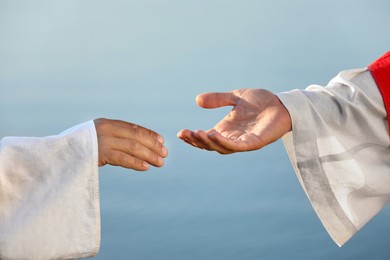 Photo of Man reaching for Jesus Christ's hand near water outdoors, closeup