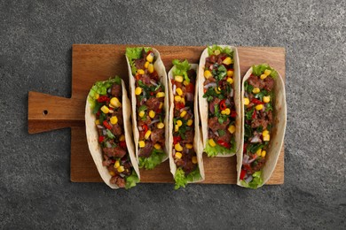 Photo of Delicious tacos with meat and vegetables on gray textured table, top view