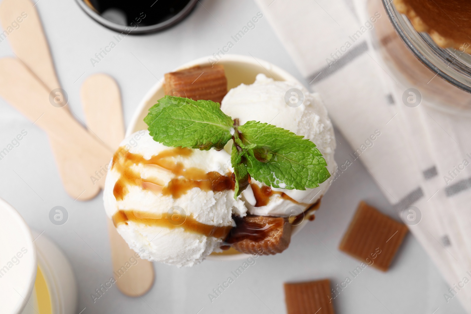 Photo of Scoops of tasty ice cream with caramel sauce, mint and candies on white table, top view