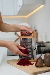 Woman grating fresh beetroot at kitchen counter, closeup