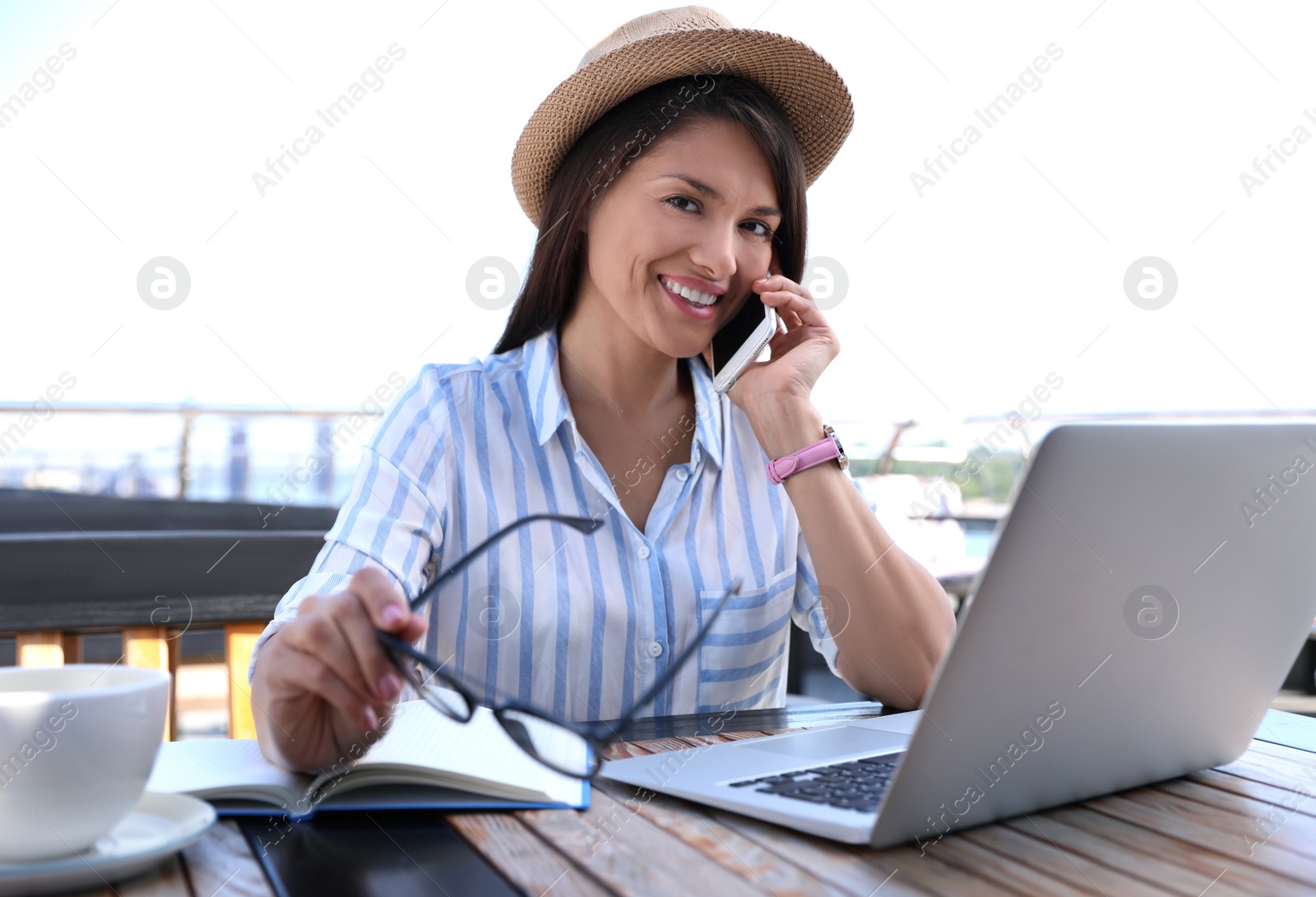 Photo of Beautiful woman with laptop talking on phone at outdoor cafe