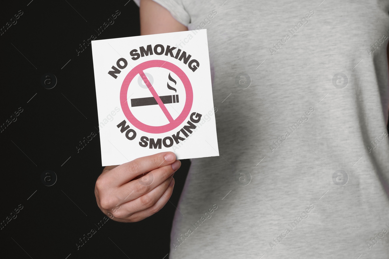 Photo of Woman holding card with no smoking sign on black background, closeup
