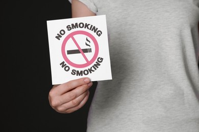 Woman holding card with no smoking sign on black background, closeup