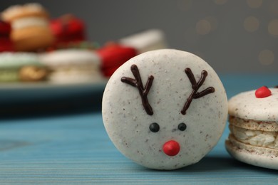 Photo of Tasty reindeer Christmas macarons on light blue wooden table against blurred festive lights, closeup