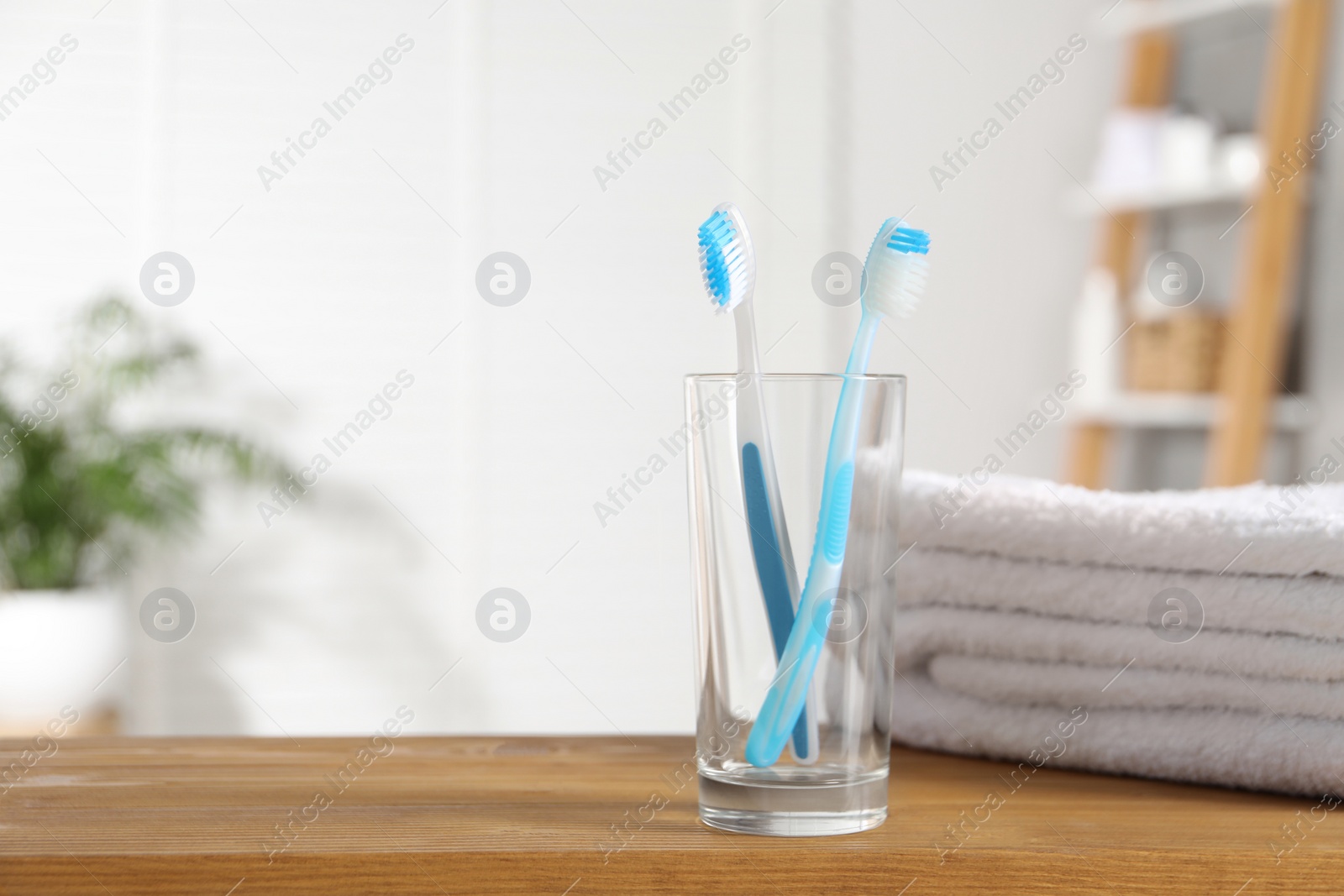 Photo of Plastic toothbrushes and towels on wooden table in bathroom, space for text