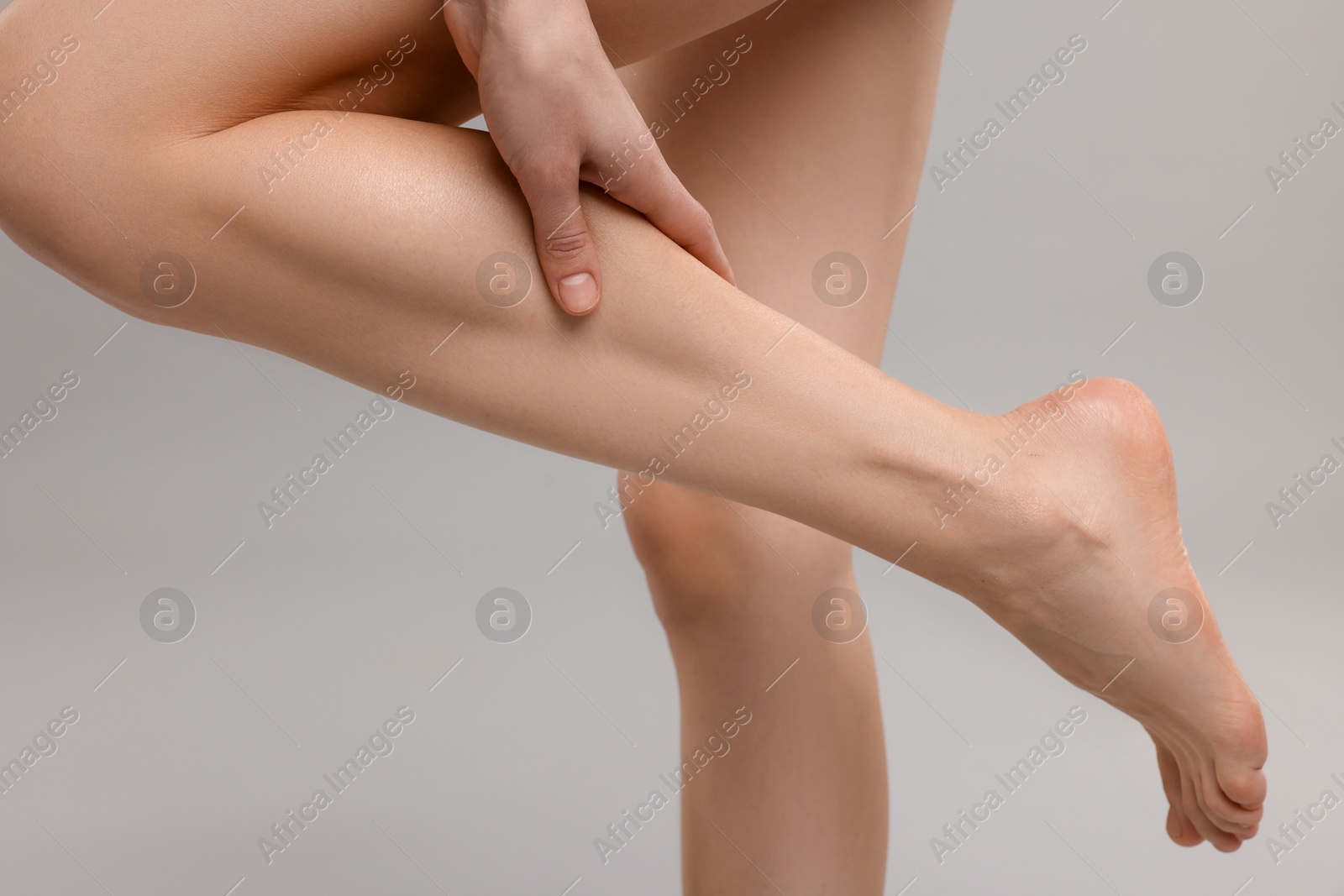 Photo of Woman suffering from leg pain on grey background, closeup