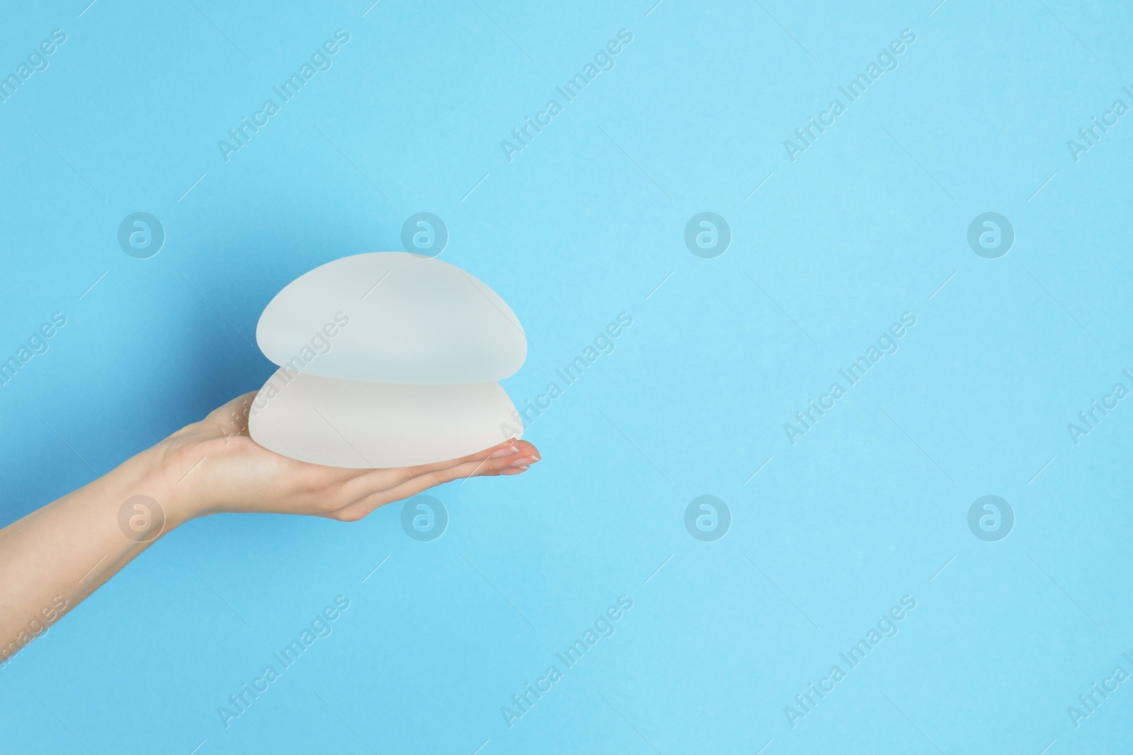 Photo of Woman holding silicone implants for breast augmentation on color background, space for text. Cosmetic surgery