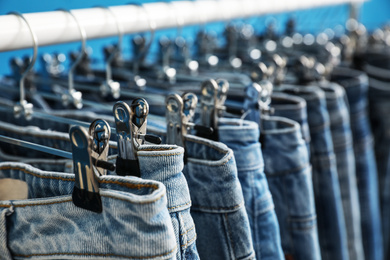 Rack with stylish jeans on blue background, closeup