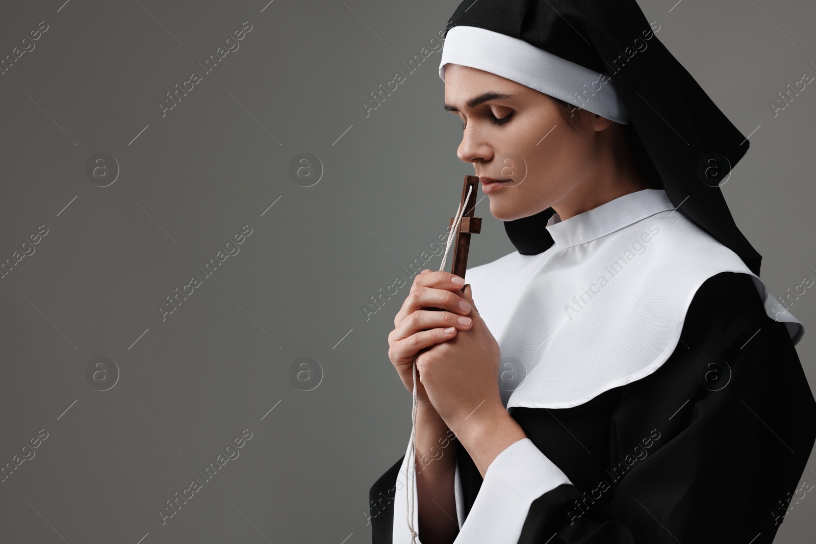 Photo of Nun with cross praying to God on grey background. Space for text