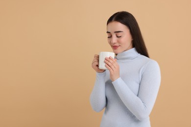 Photo of Beautiful young woman holding white ceramic mug on beige background, space for text