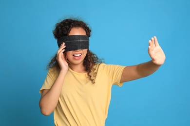 Photo of Young African-American woman with black blindfold on blue background