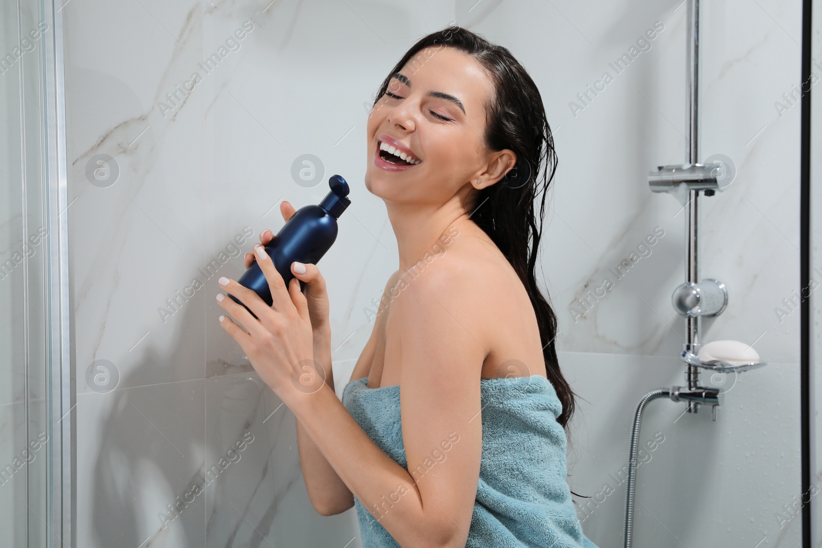 Photo of Young woman with bottle of gel singing while taking shower