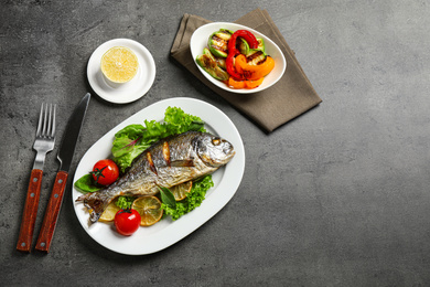 Photo of Delicious roasted fish with lemon on dark grey table, flat lay