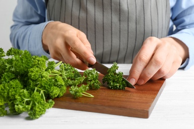 Photo of Woman cutting curly parsley at white wooden table, closeup