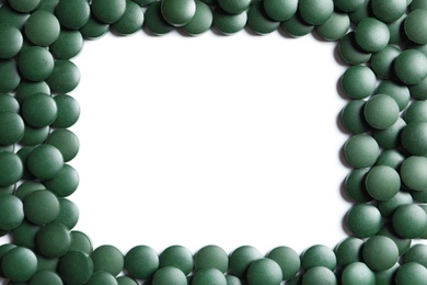Photo of Frame made of green spirulina pills on white background, top view with space for text