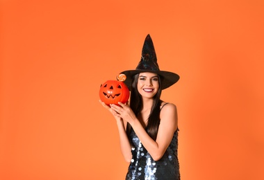 Photo of Beautiful woman wearing witch costume with Jack O'Lantern candy container for Halloween party on yellow background, space for text