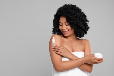 Young woman applying body cream onto shoulder on grey background. Space for text