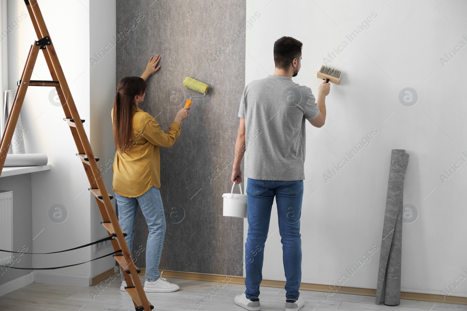 Photo of Woman and man hanging wallpaper in room, back view