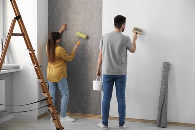 Photo of Woman and man hanging wallpaper in room, back view