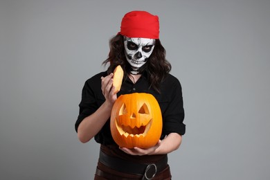 Photo of Man in scary pirate costume with skull makeup and carved pumpkin on light grey background. Halloween celebration