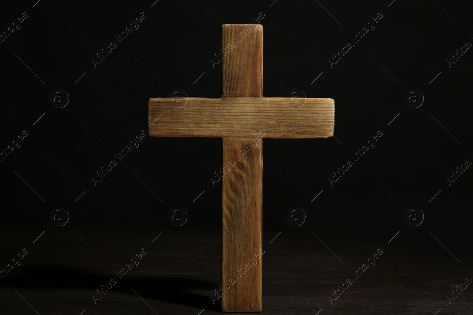 Photo of Christian cross on wooden table against black background. Religion concept